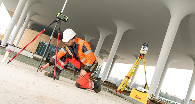 Un ouvrier de chantier marque des points sur le sol dans le cadre d’un projet de construction de bâtiment avec une station totale robotisée Leica iCON iCR70 pendant l’implantation.